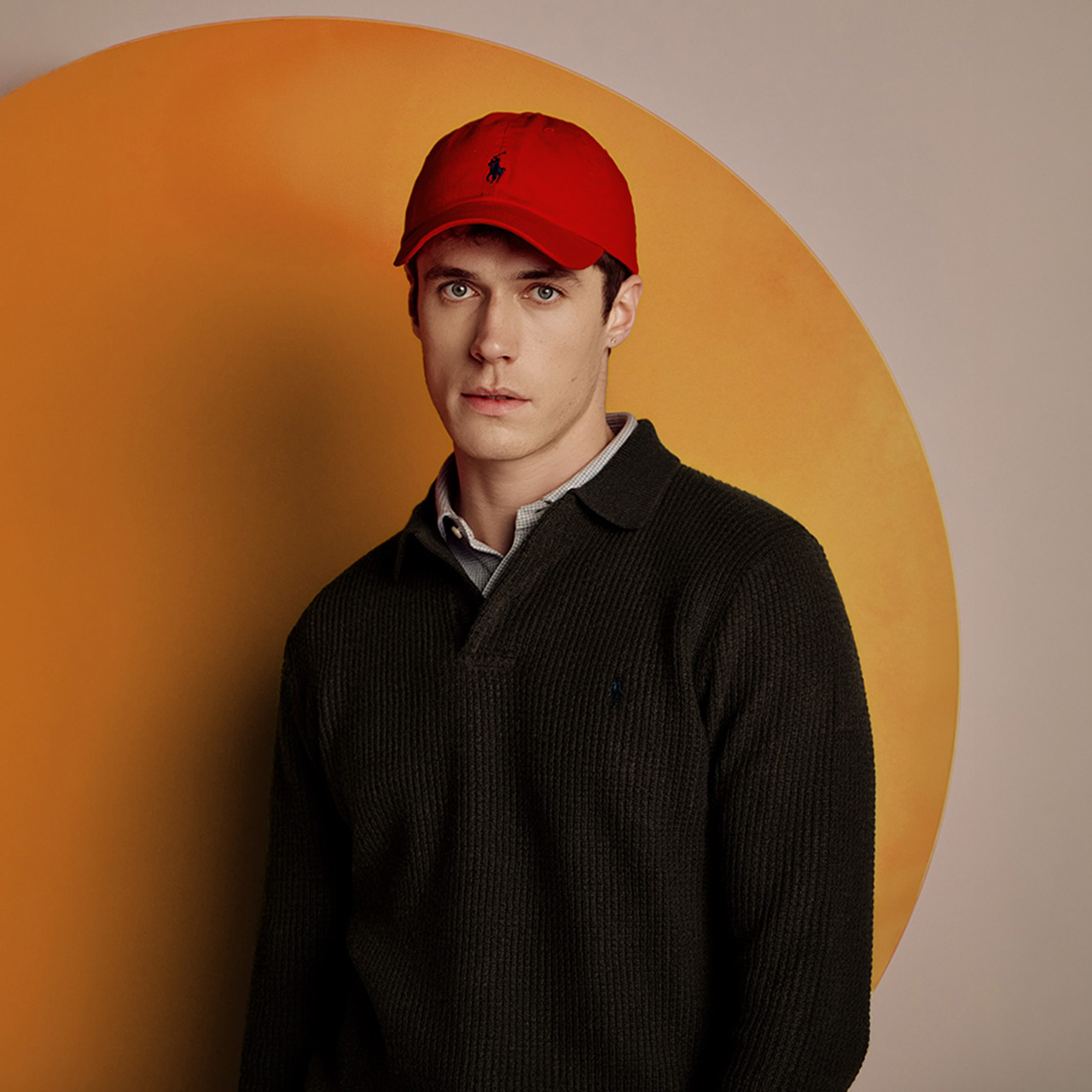 A person wearing a red cap and dark sweater stands in front of a large red circle.